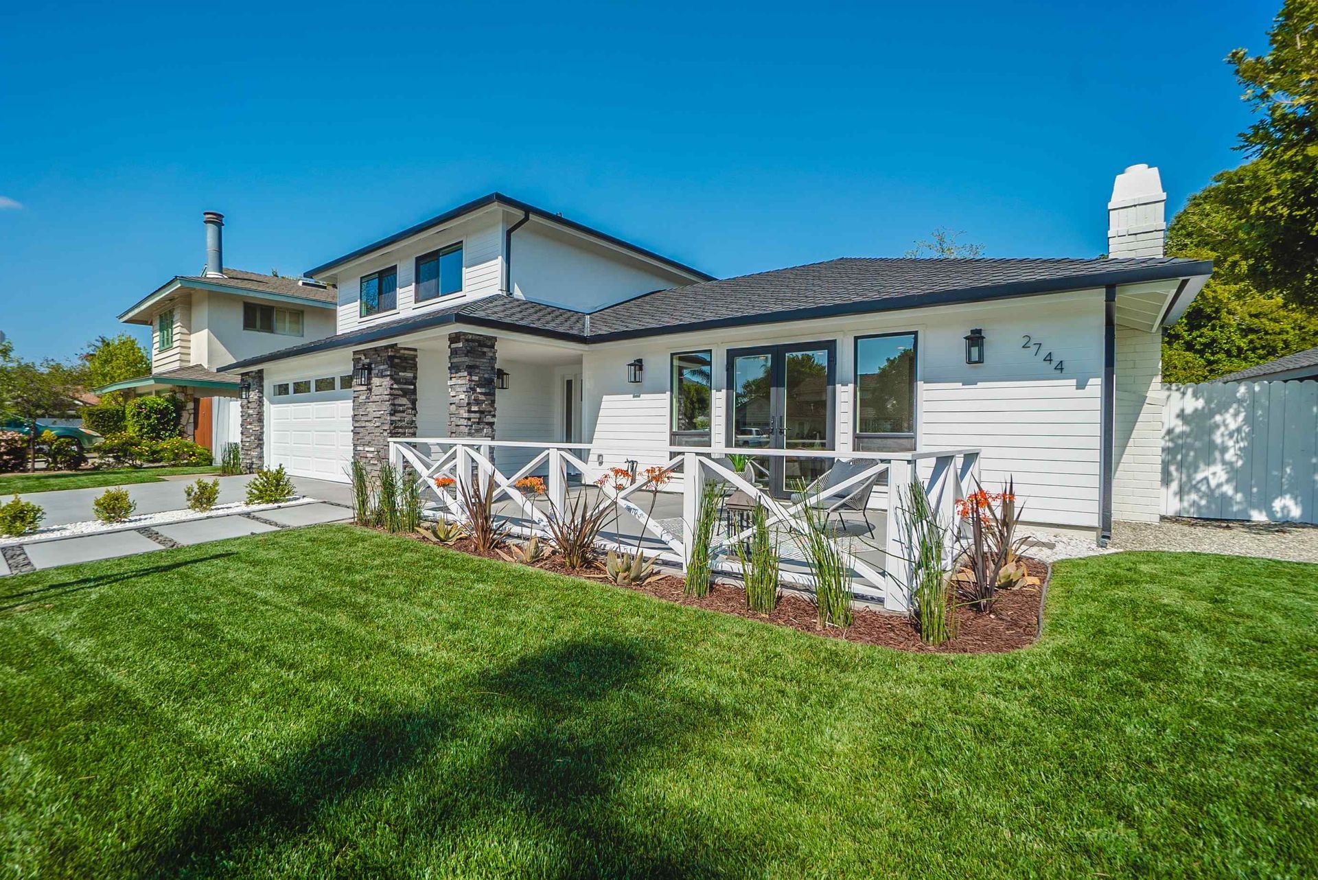 Modern white house with black accents and manicured lawn on a sunny day.