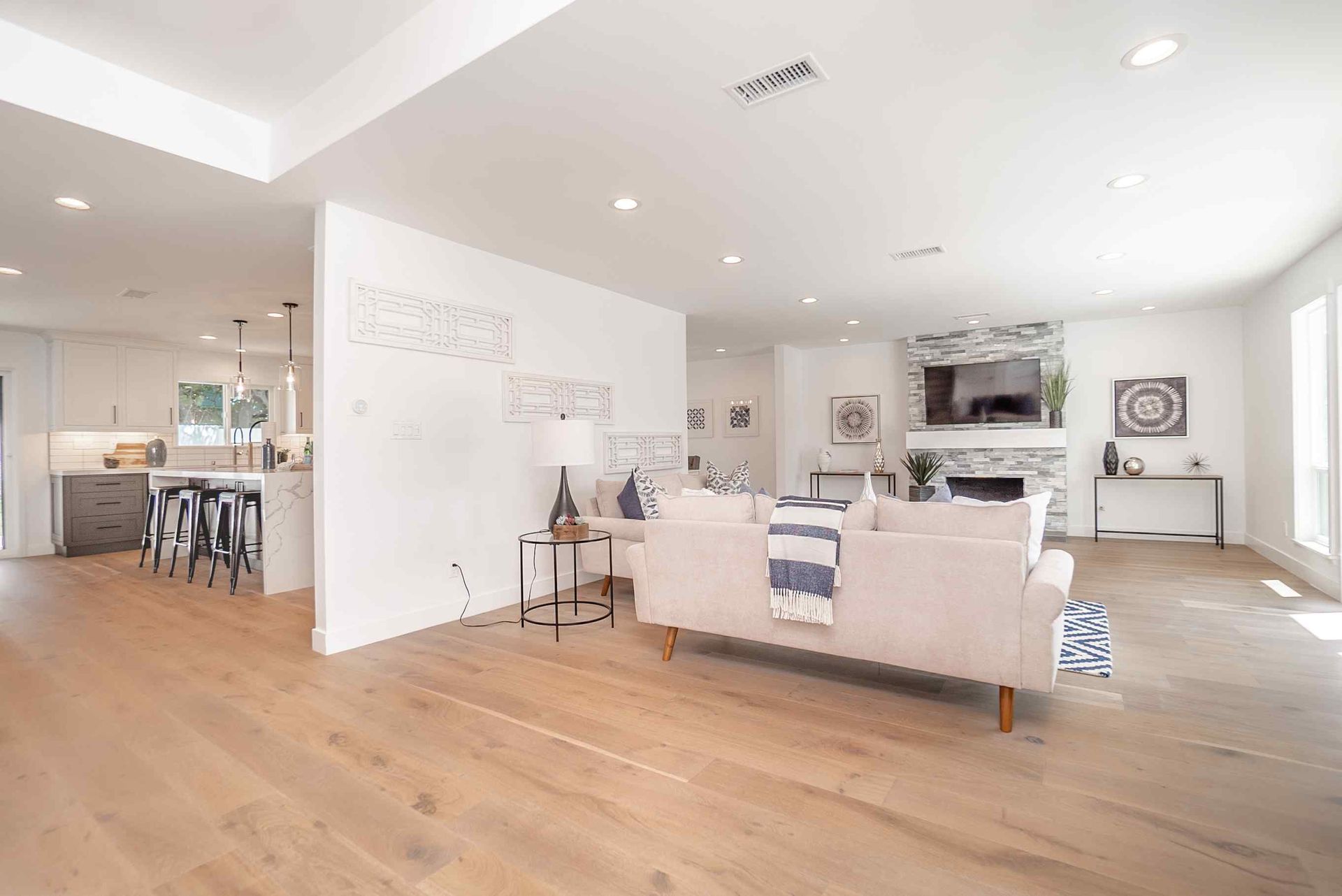 Open-concept living space with hardwood floors, white walls, a fireplace, and a kitchen in the background.