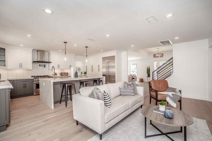 Open-concept kitchen and living room with white and gray cabinets, light wood floors, and modern furniture.