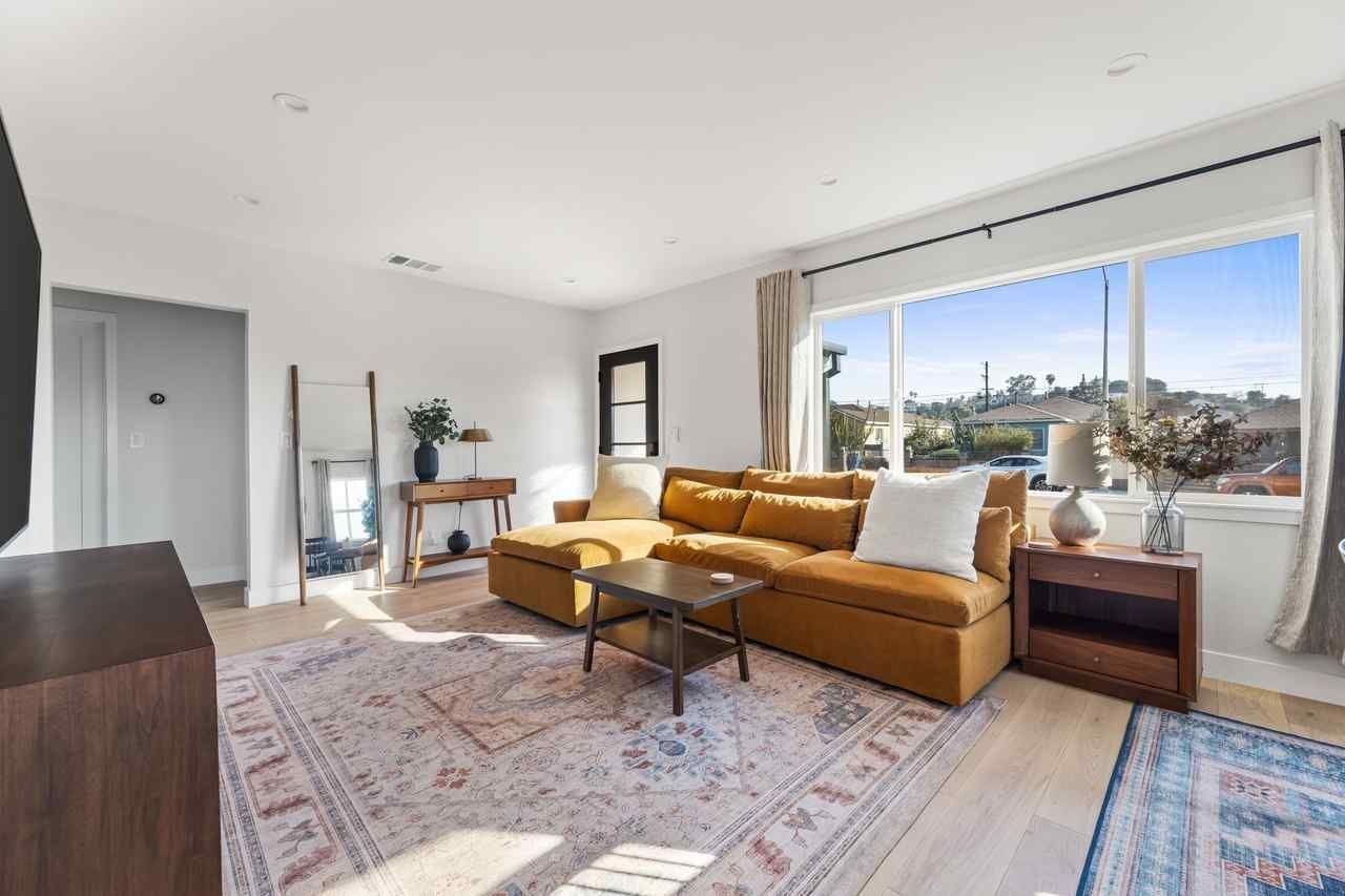 Living room with a mustard-colored sectional, rug, large window, and a small coffee table.