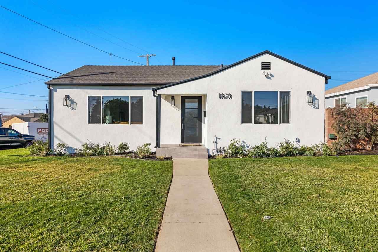White stucco bungalow with black trim, front lawn, sidewalk, blue sky.