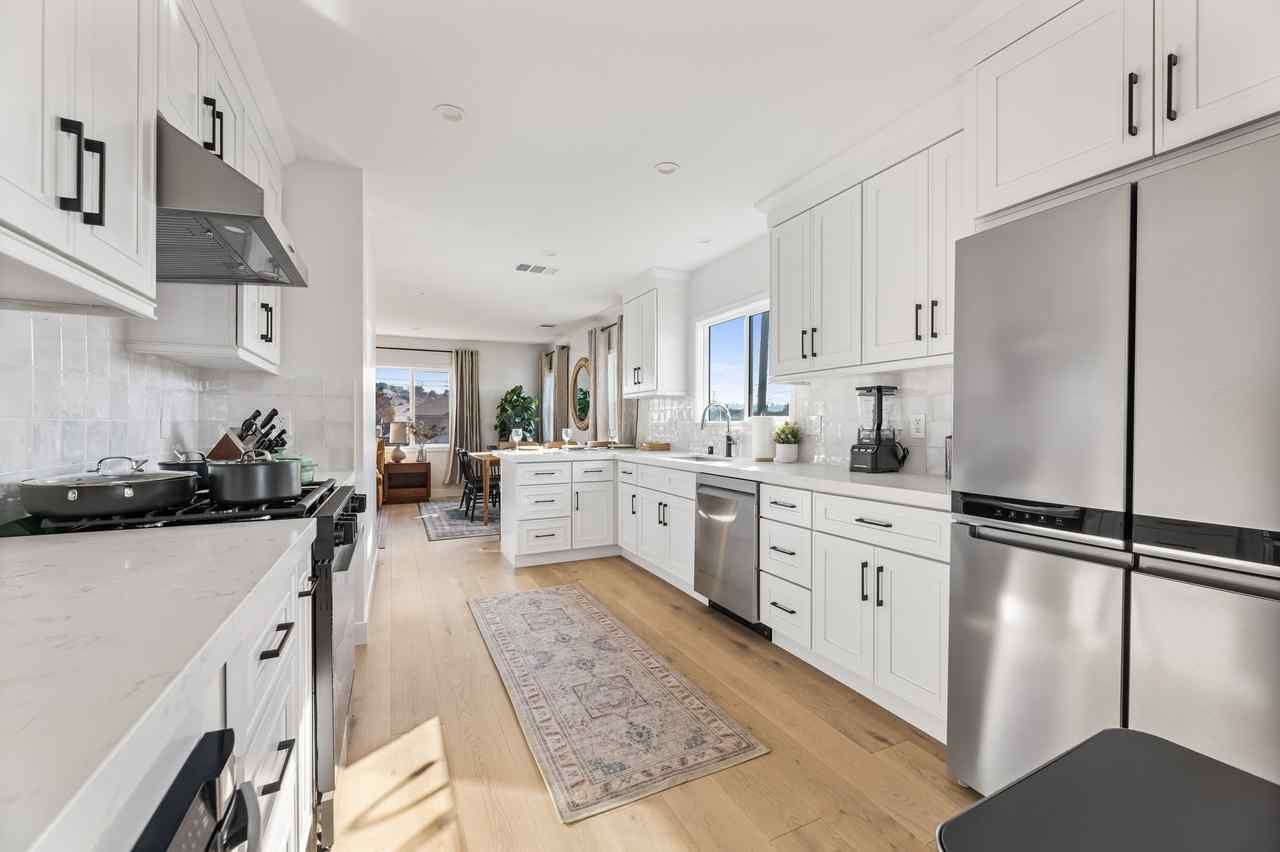 Modern white kitchen with stainless steel appliances and light wood floors.