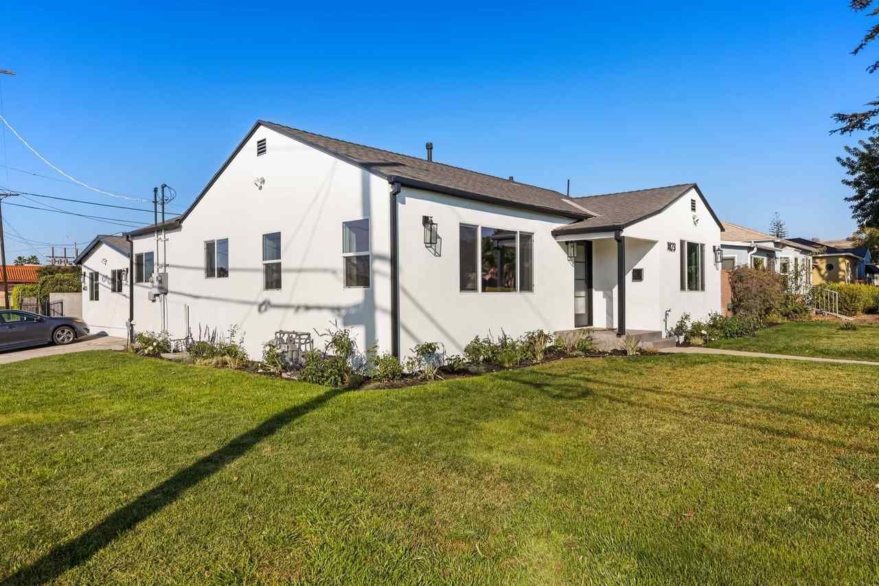 White house with black trim and a green lawn under a blue sky.