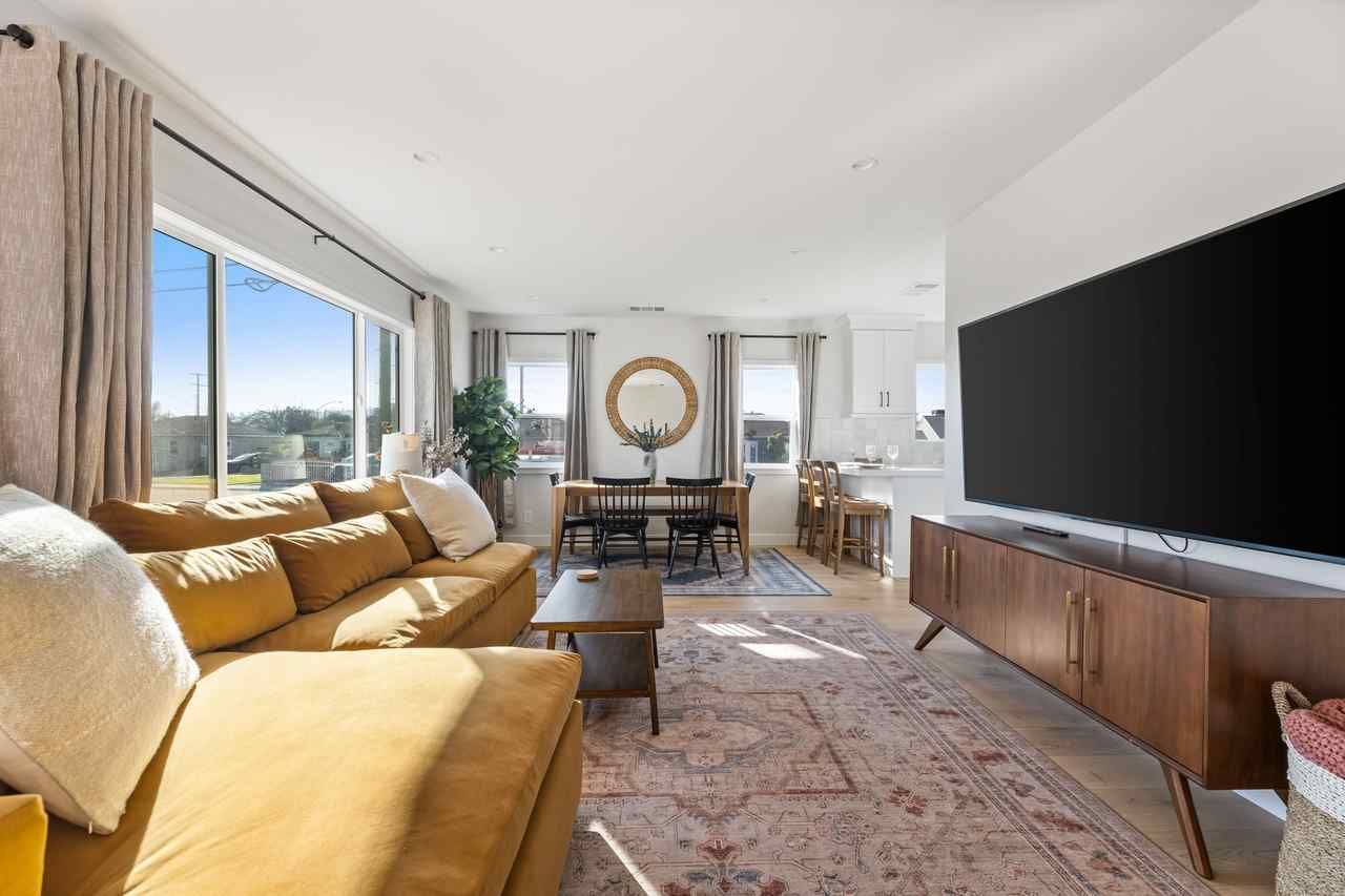 Mustard-colored sectional sofa in a bright living room with large windows and a mounted TV.