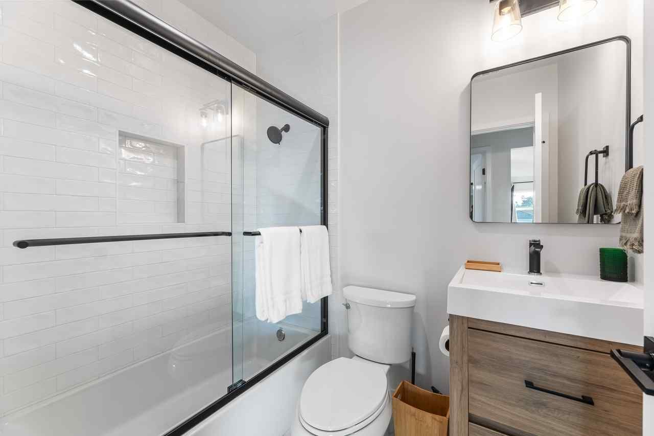 Bathroom with a white toilet, sink, shower, and gray walls. A dark-framed mirror hangs above the sink.