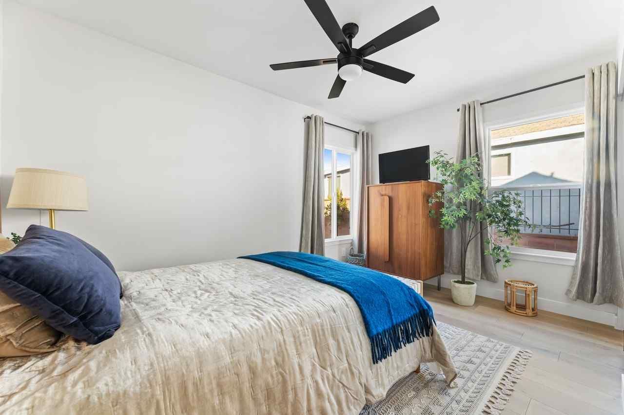 Bedroom with a bed, windows, TV on a wooden cabinet, and a ceiling fan.