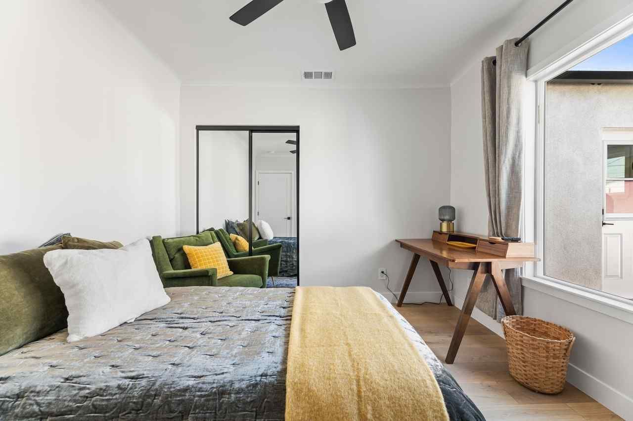 Bedroom with bed, green sofa, desk by window, neutral colors.