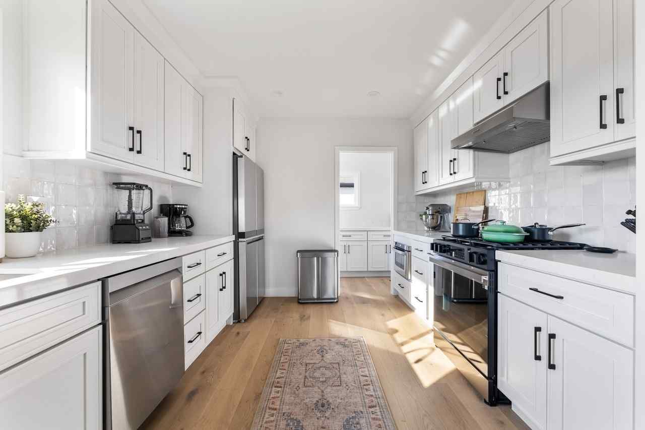 Bright white kitchen with stainless steel appliances, black hardware, and light wood floors.