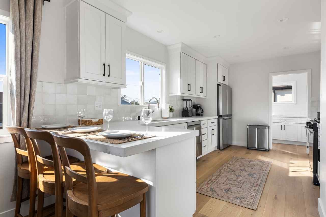 White kitchen with breakfast bar and wooden stools, stainless steel appliances, and hardwood floors.