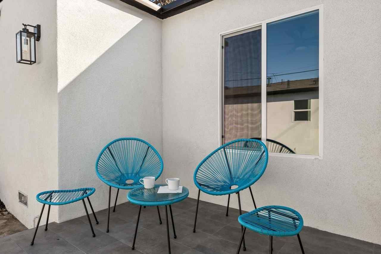 Small patio with turquoise chairs and a small table. White walls, dark window.