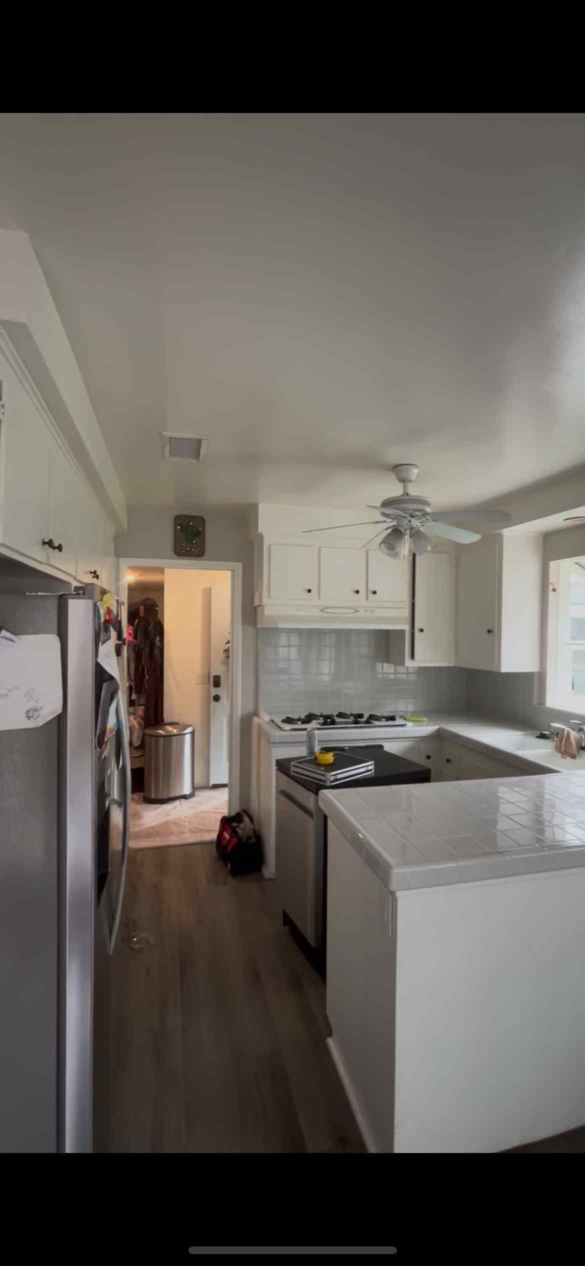 A bright, white kitchen with stainless steel appliances and a U-shaped countertop. Light wood floors.