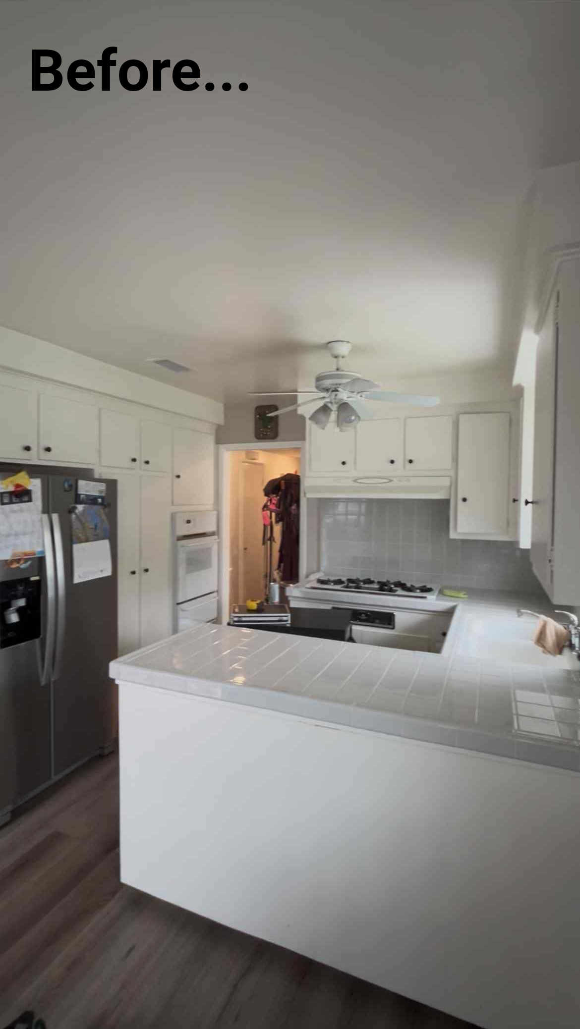White kitchen before renovation: white cabinets, counters, and appliances; view toward a doorway.