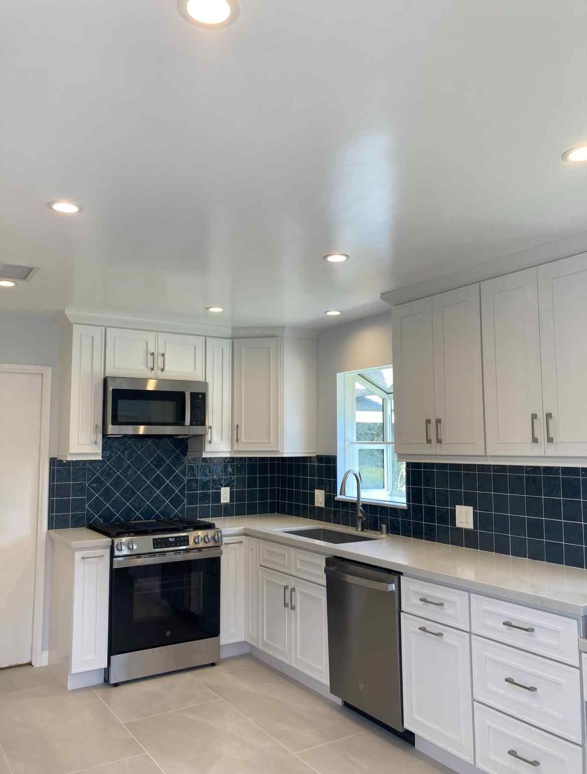 Modern kitchen with white cabinets, stainless steel appliances, and blue backsplash.