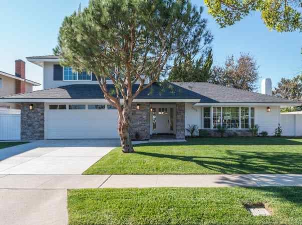 Mid-century modern house with a tree in the front yard; white exterior, gray stone accents, and a green lawn.