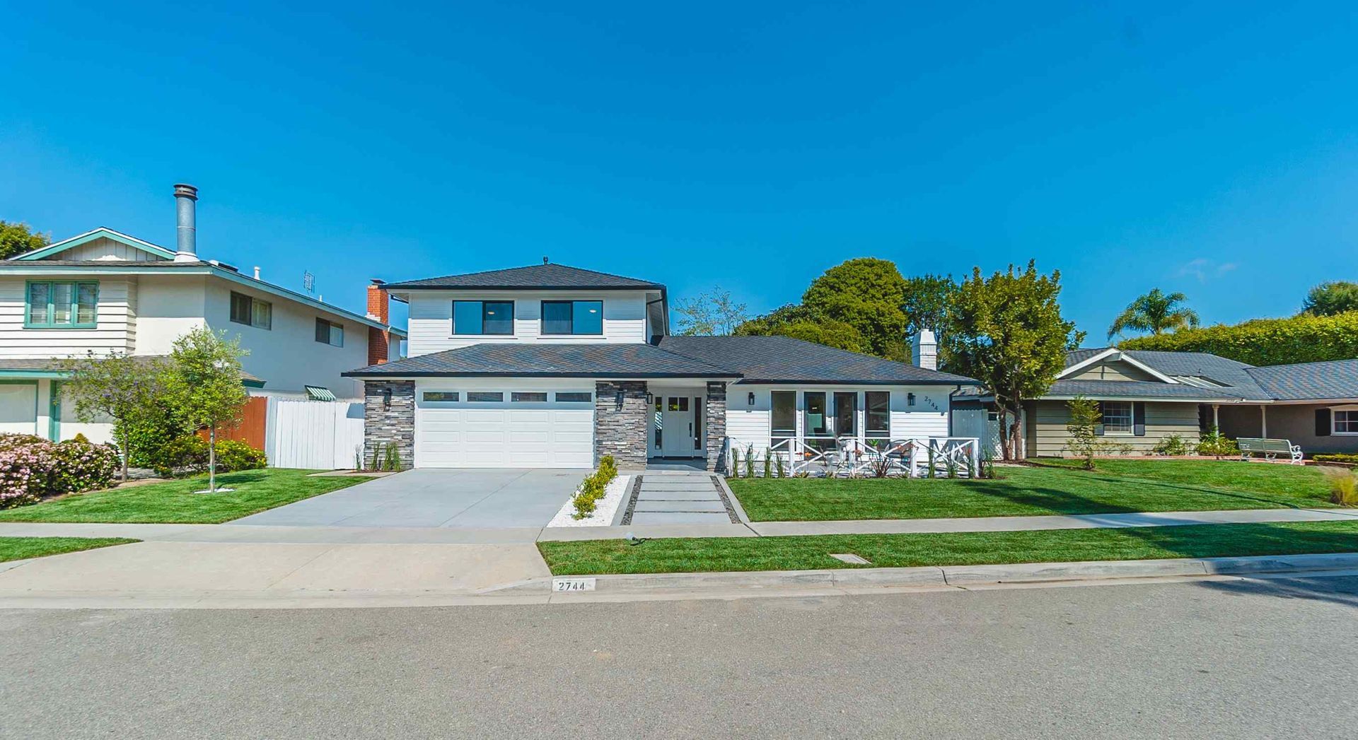 Modern white house with a gray driveway, green lawn, and blue sky.