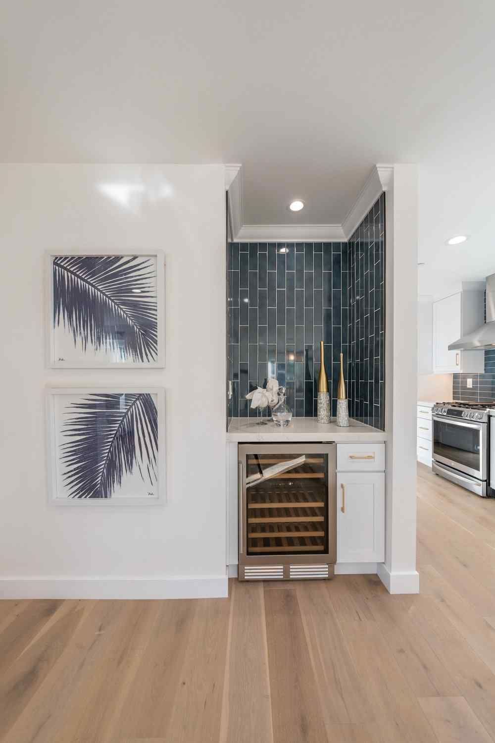 Built-in bar area with wine fridge, blue tile backsplash, and framed botanical prints; light wood floor.