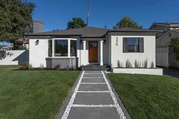 White house with a gray roof and walkway, framed by grass and bushes.