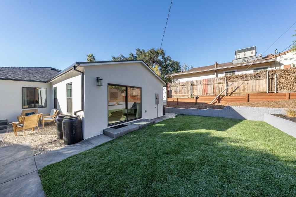 Backyard with a white house, green lawn, patio, and a wooden fence on a sunny day.