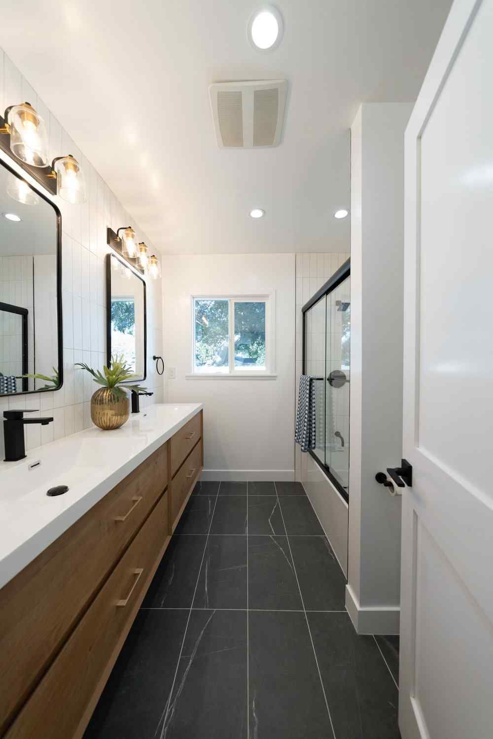 Modern bathroom with double vanity, black fixtures, dark tiled floor, and shower.