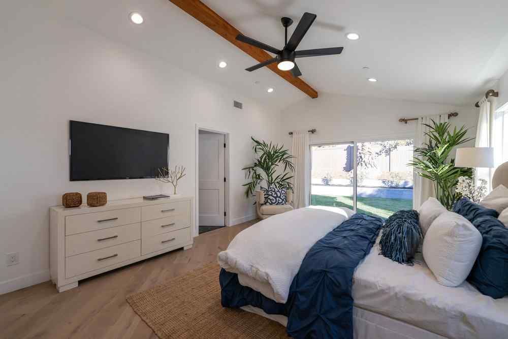 Bright, modern bedroom with a bed, TV, plants, and a view of the yard.