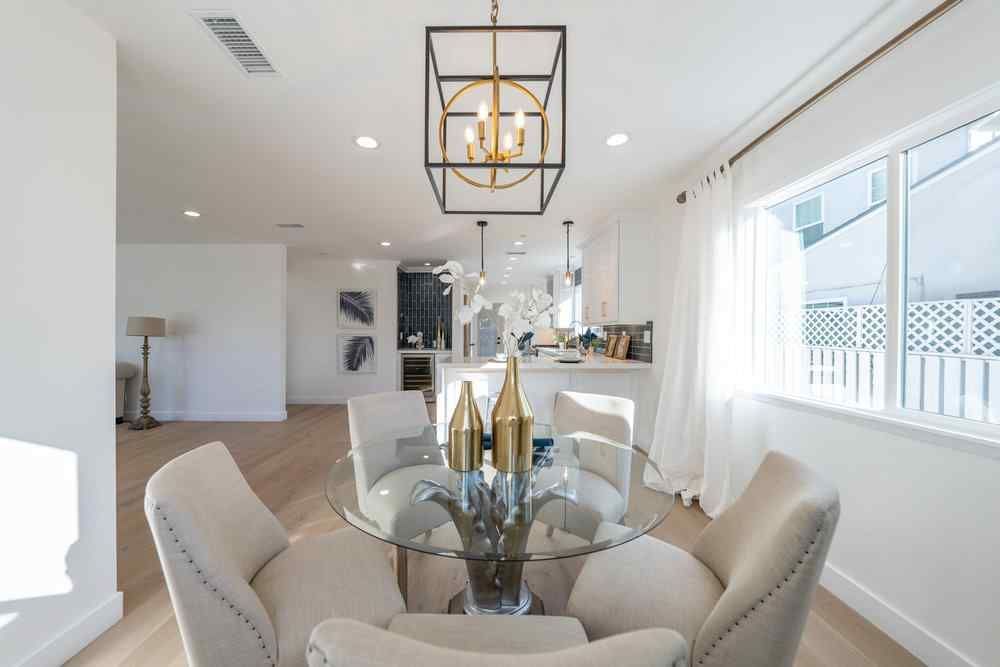 Dining room with glass table, upholstered chairs, and gold accents; view into kitchen area.
