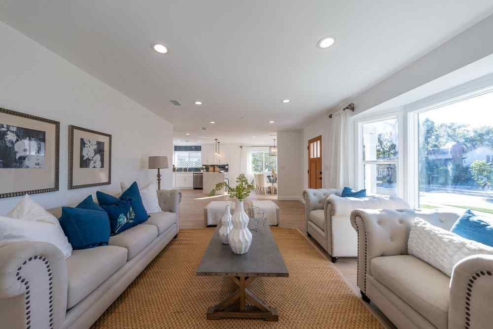 Cozy living room with white sofas, blue pillows, and a wooden coffee table, leading to the kitchen.