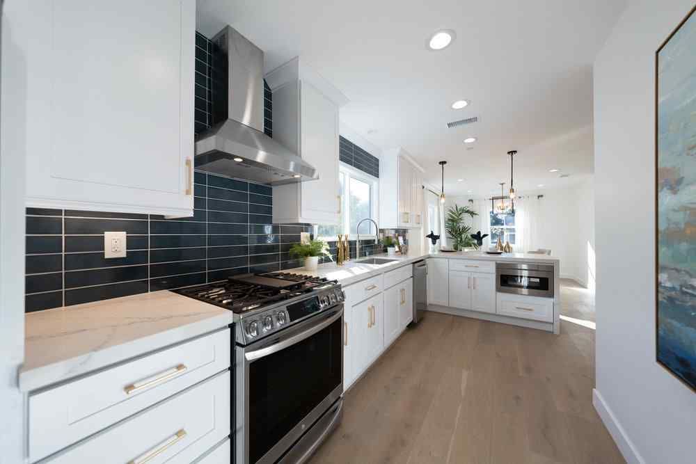 Modern kitchen with white cabinets, stainless steel appliances, and blue tiled backsplash.