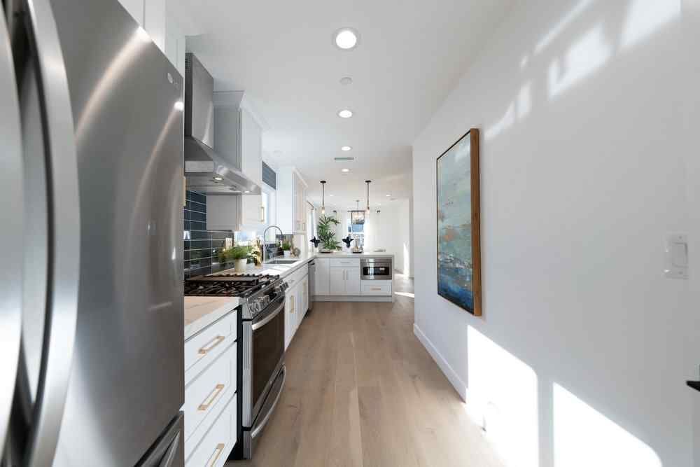 Long, narrow kitchen with stainless steel appliances, white cabinets, and light wood floors.