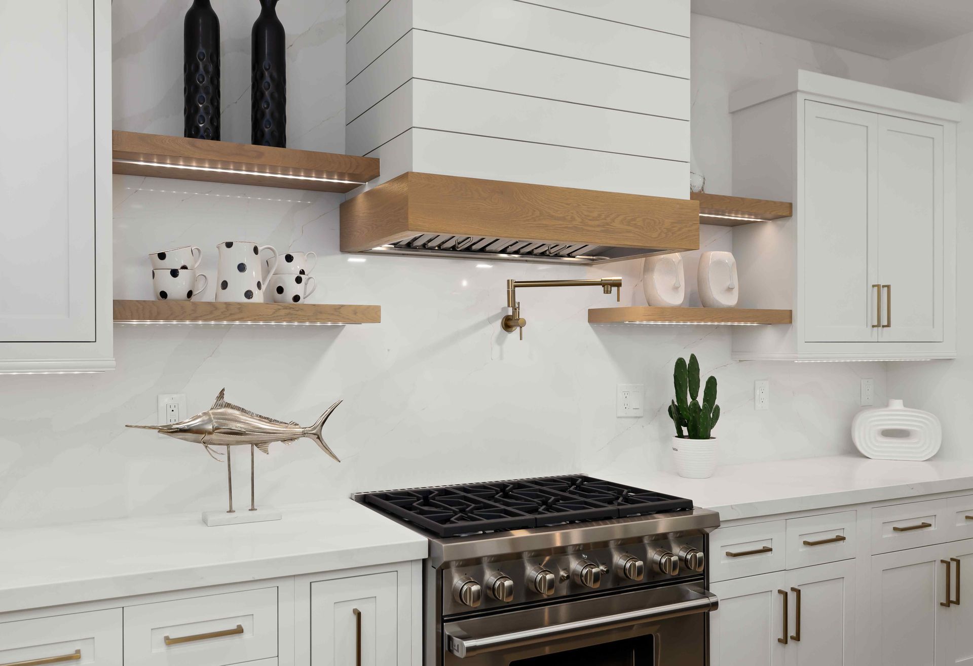 White kitchen with stainless steel stove, range hood, and floating wooden shelves.