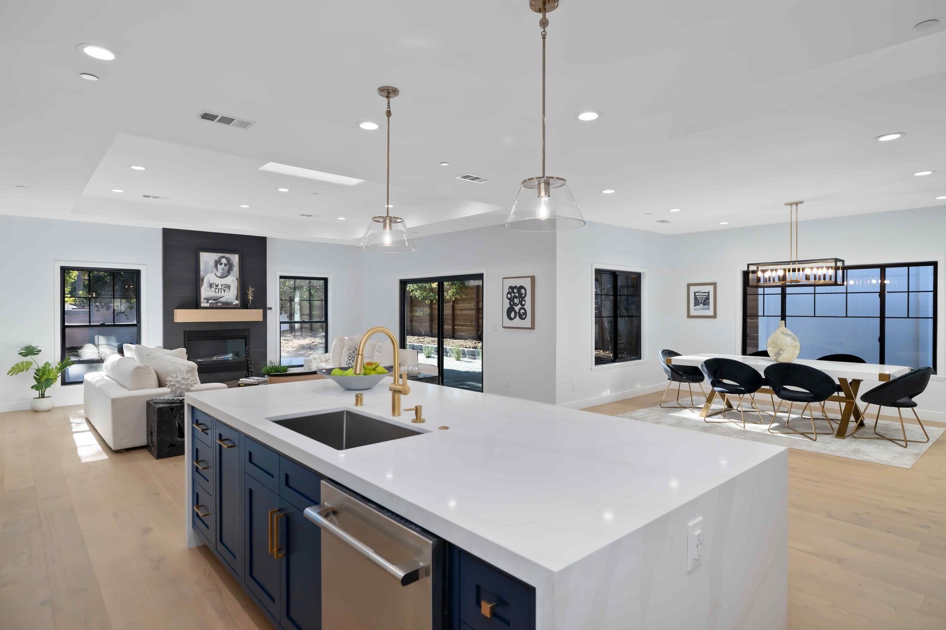 Open-concept kitchen and living space with blue island, white countertops, and dining area with black chairs.