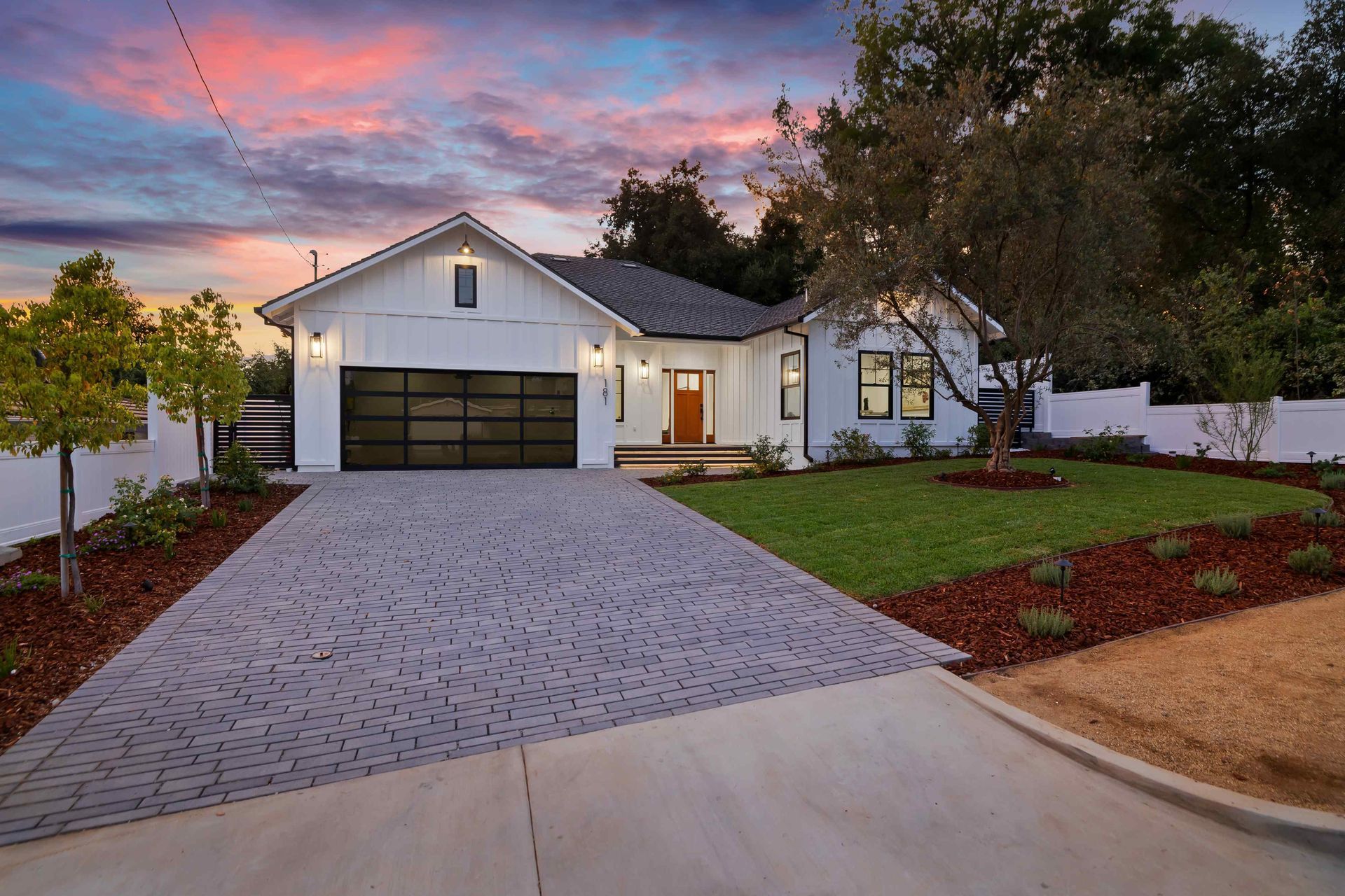 White farmhouse with black garage door, brown door, and paved driveway; sunset sky.