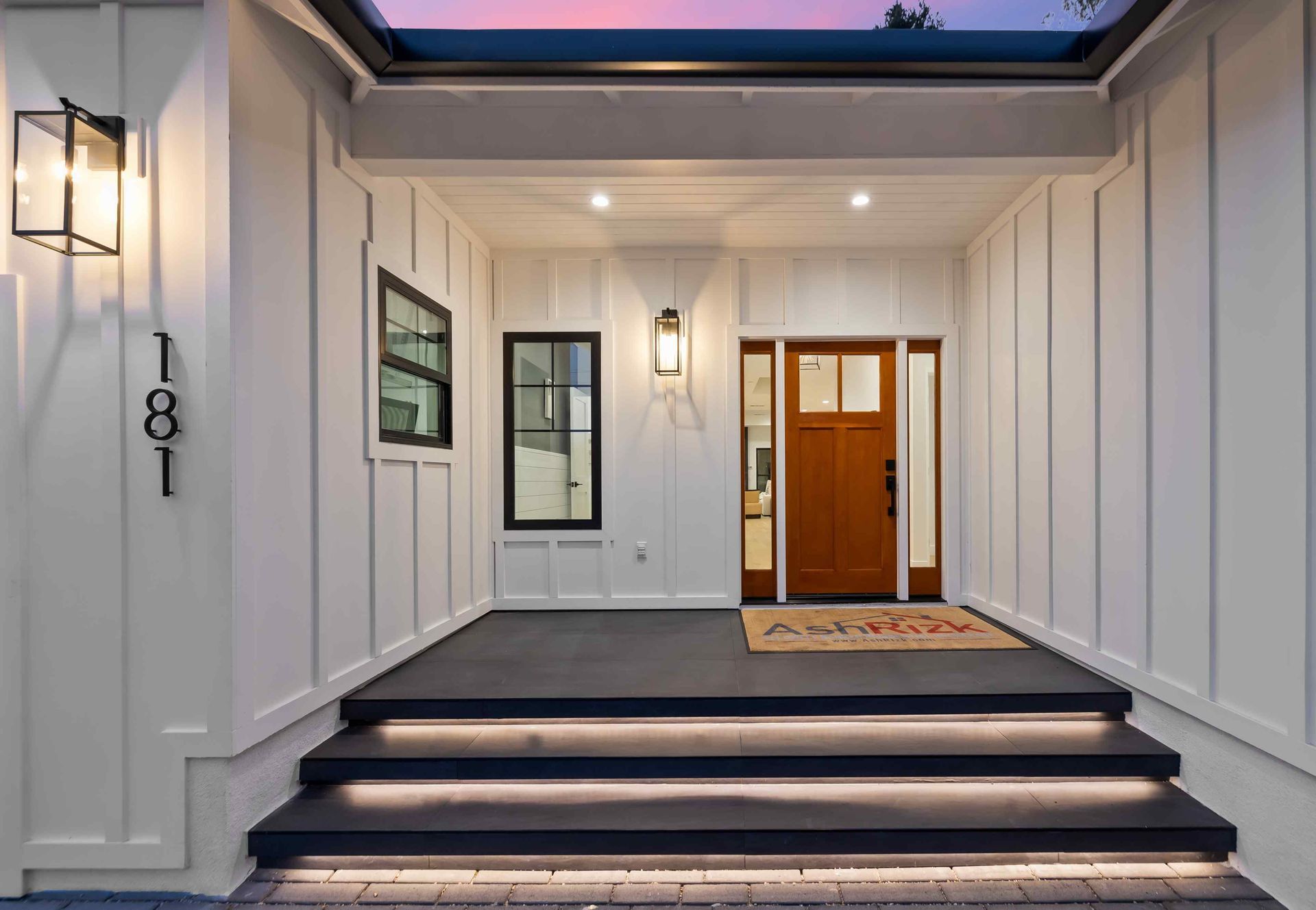 White house with black trim and patio, lush green lawn.