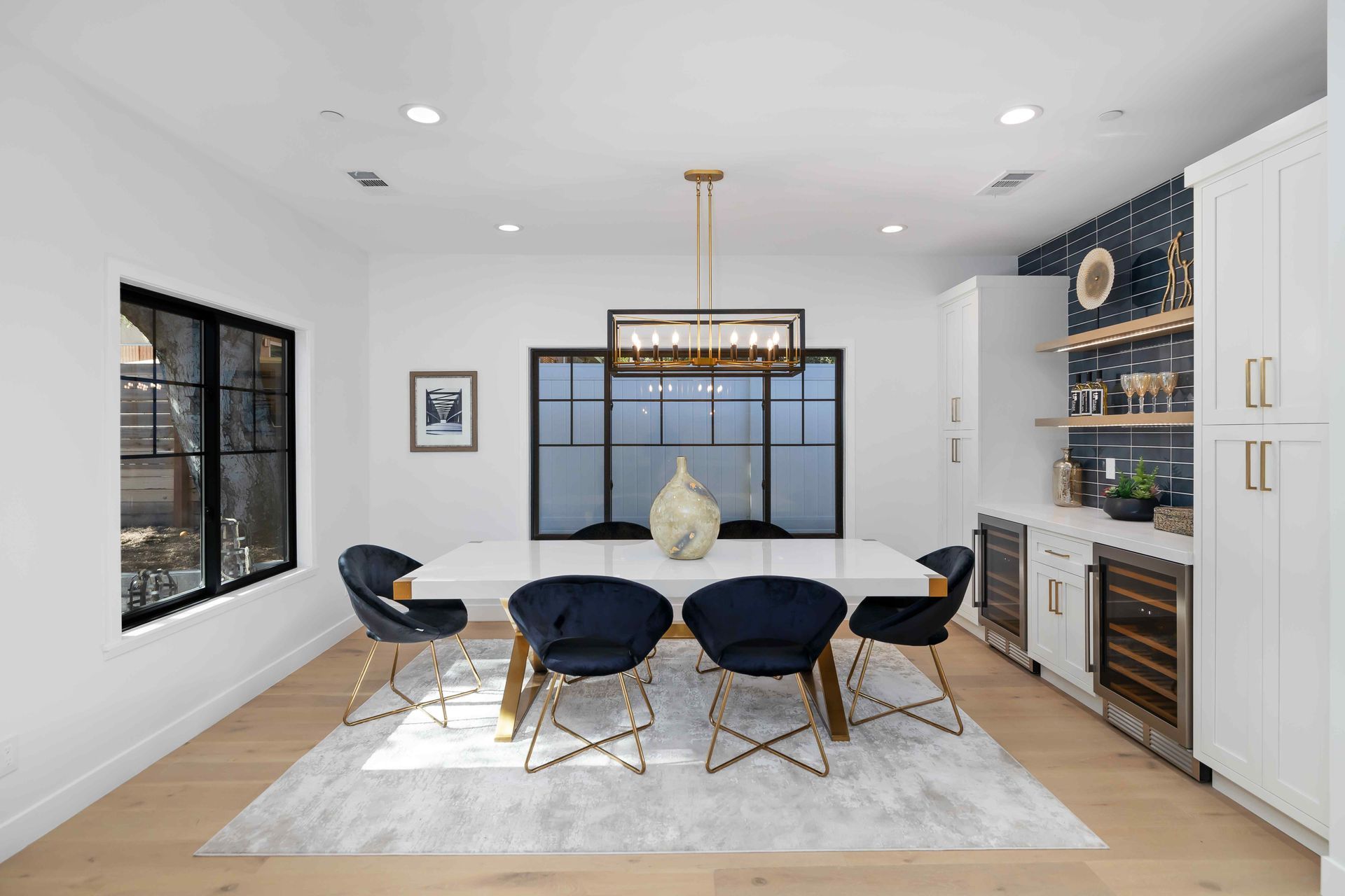 Modern dining room with white table, navy chairs, gold accents, and a built-in bar.