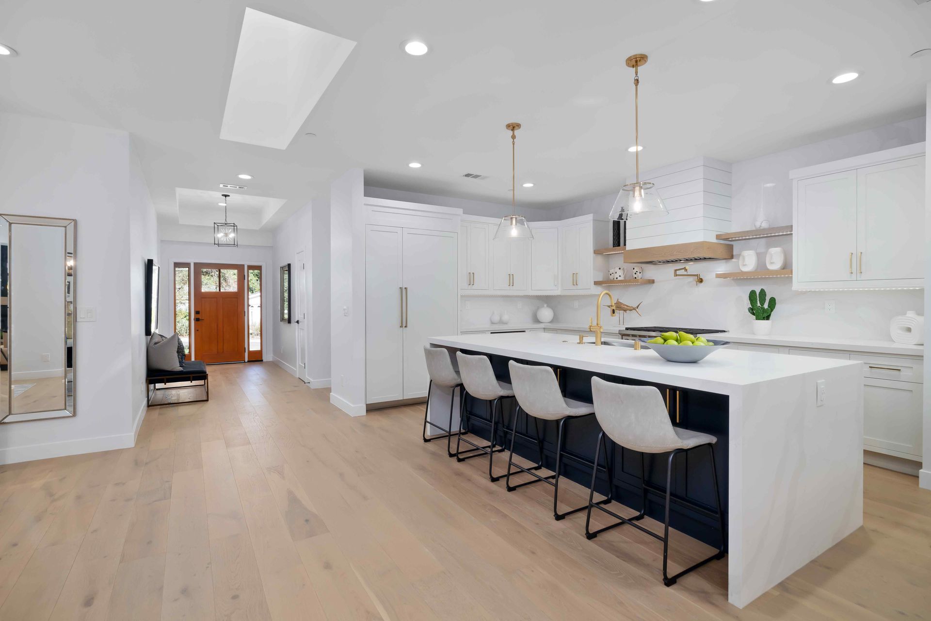 Spacious white kitchen with a navy island, light wood floors, and a view to the front door.