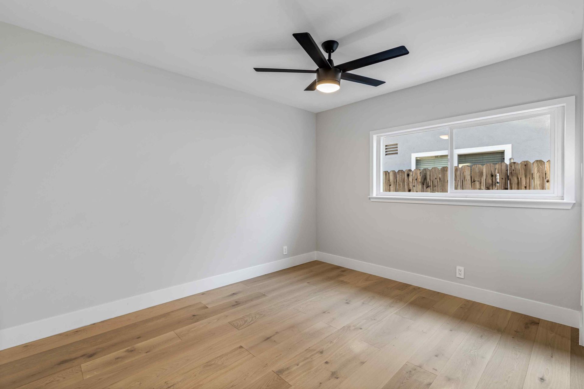 Empty room with light wood floors, gray walls, ceiling fan, and a window.