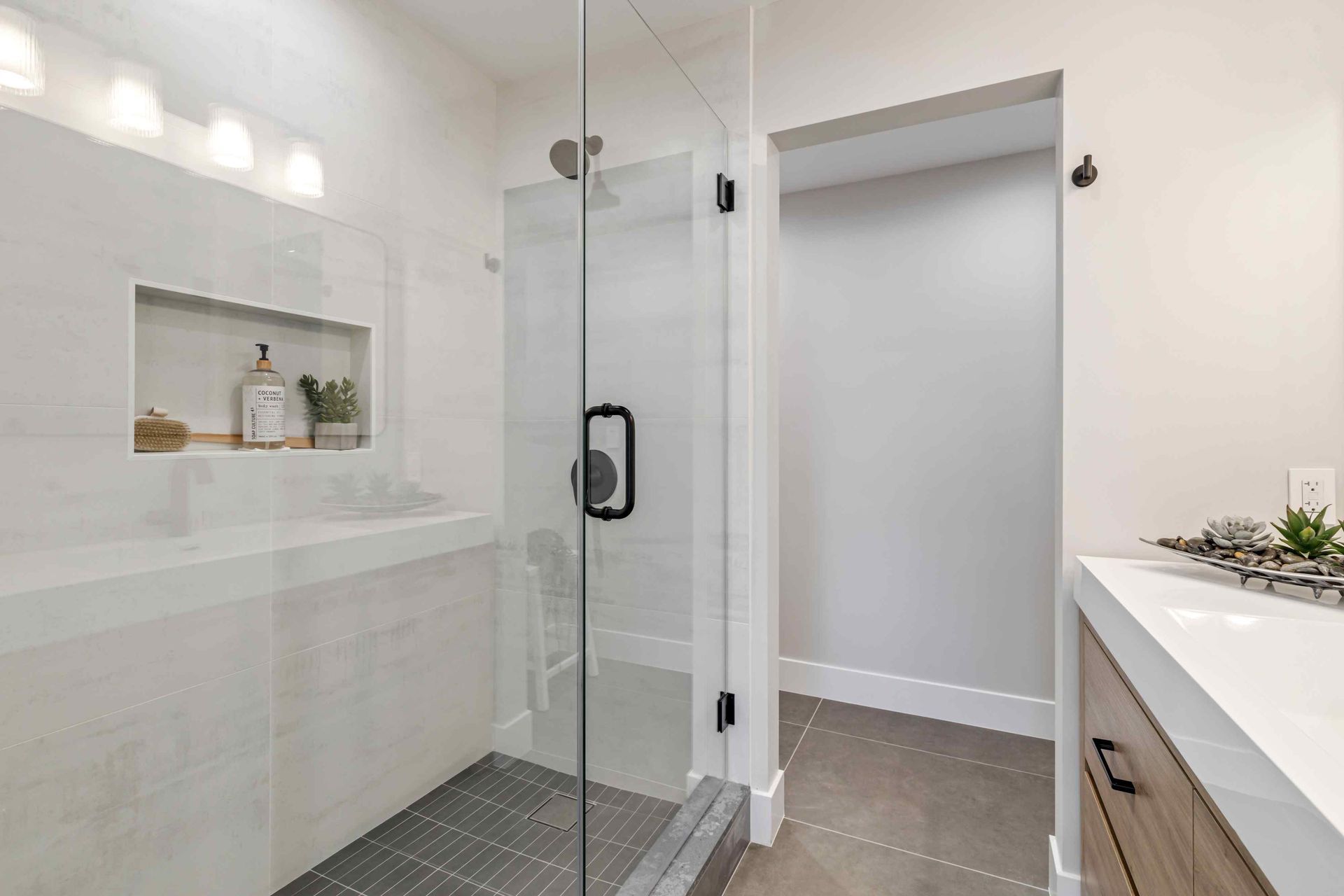 Modern bathroom with glass shower, white walls, and gray floor tiles.