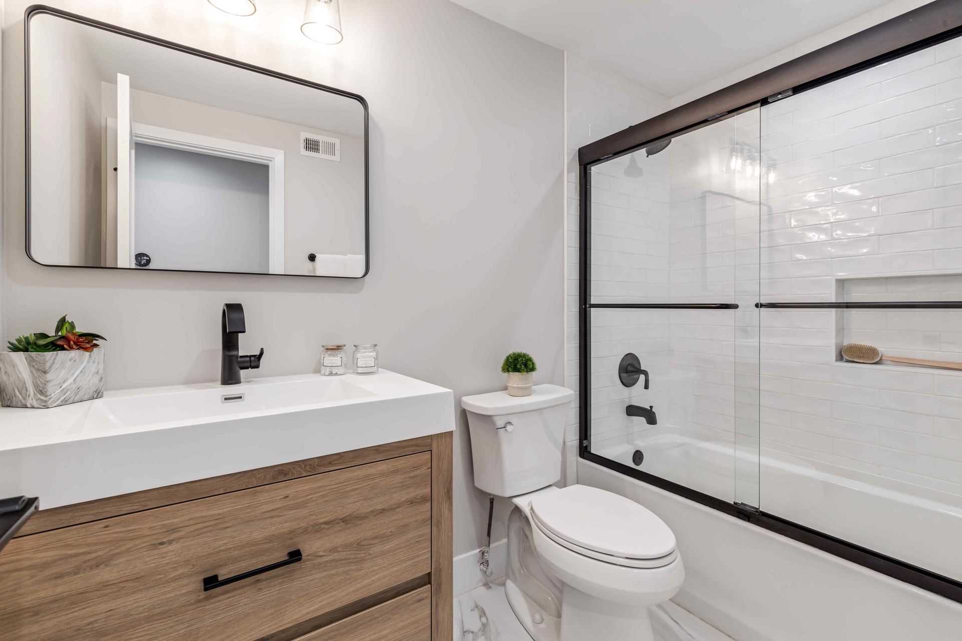 Modern bathroom with wood vanity, white sink, toilet, and a glass-enclosed shower.