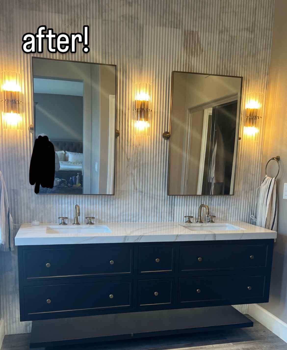 Modern bathroom with floating navy vanity, two mirrors, gold sconces, and textured wall.