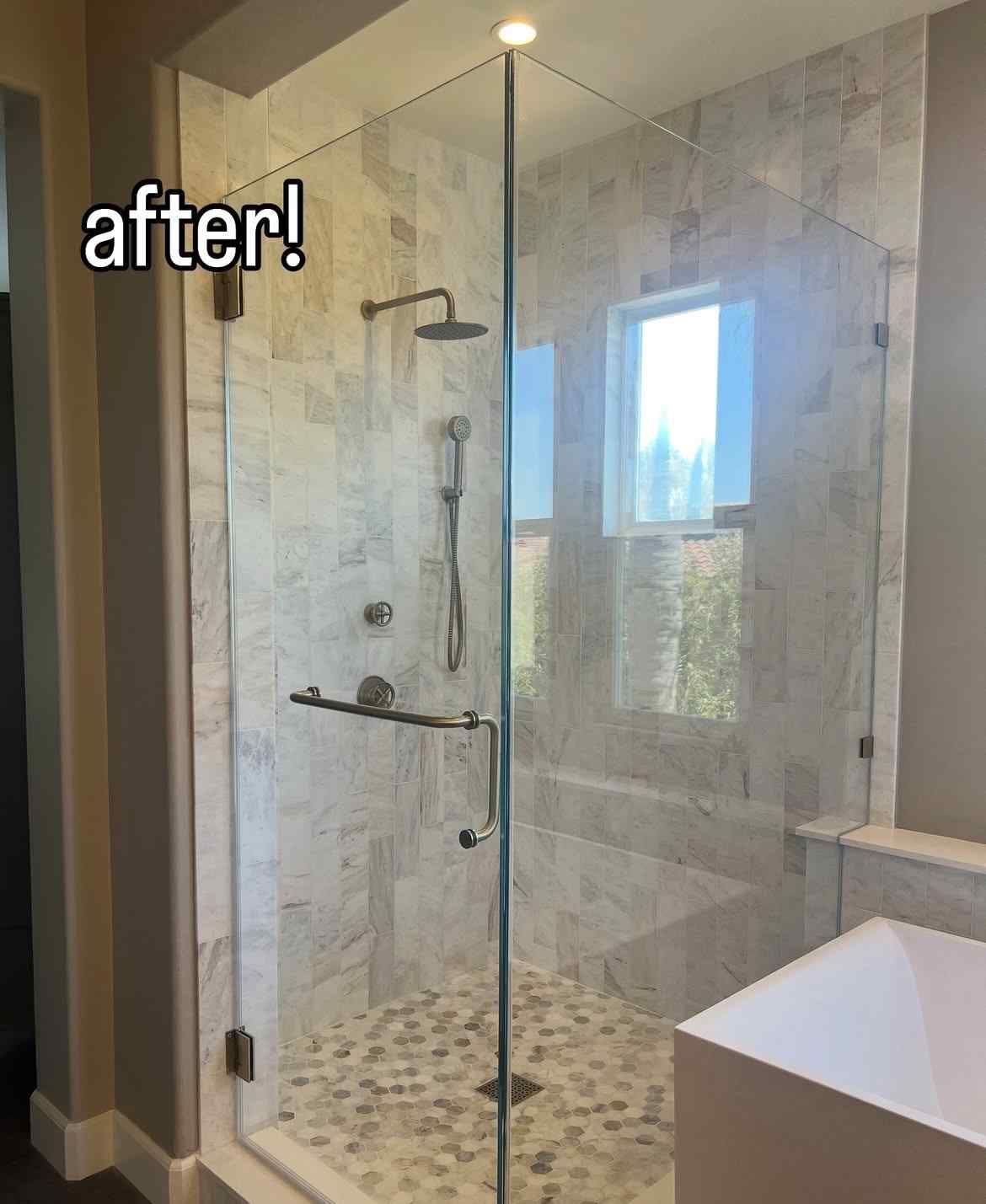Glass shower enclosure with marble tile, pebble floor, and white tub.