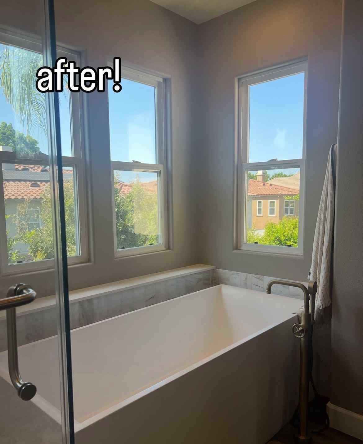 Modern bathroom with a white bathtub, windows, and towel hanging on the wall.