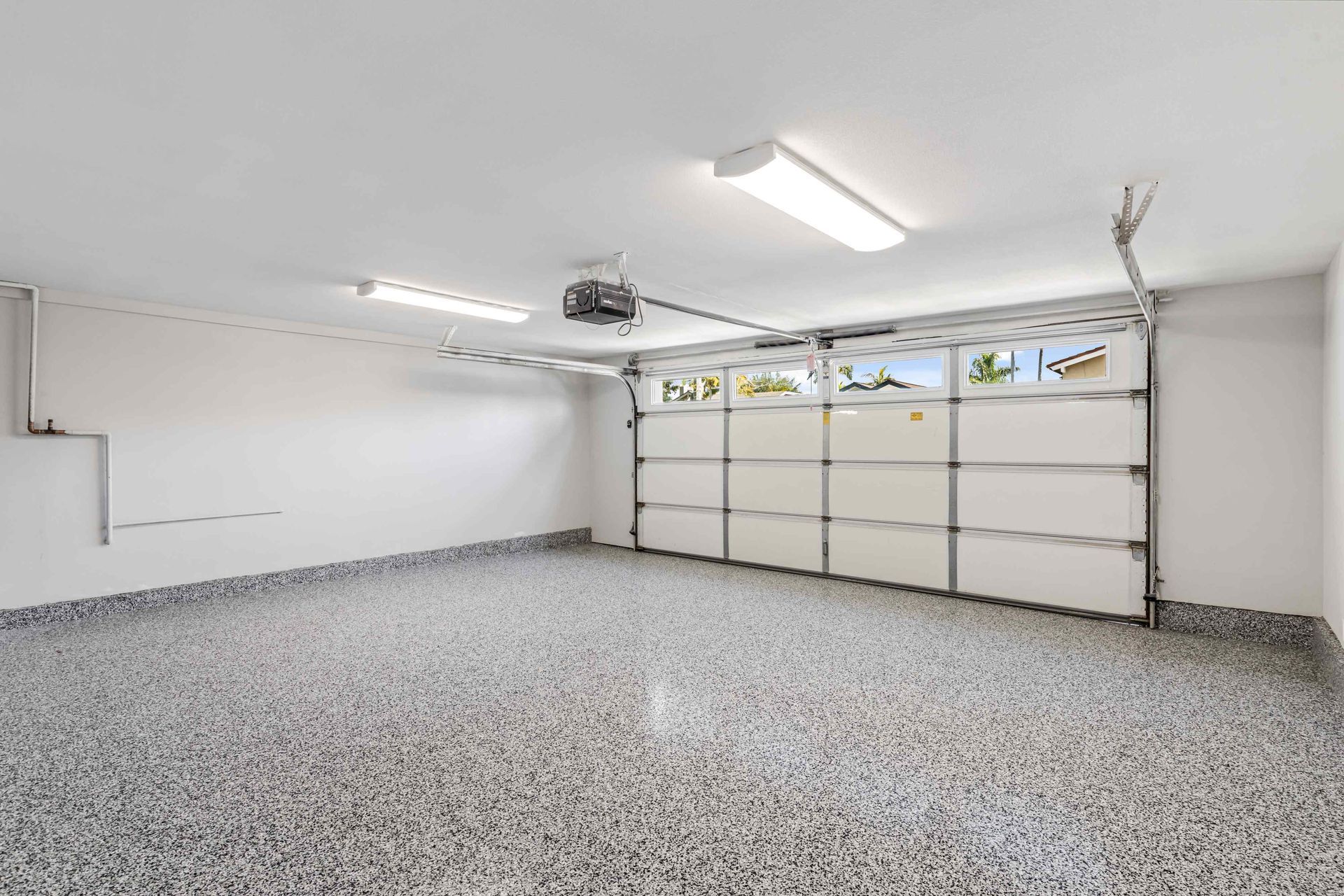 Empty garage with gray speckled floor, closed white door, and overhead lights.