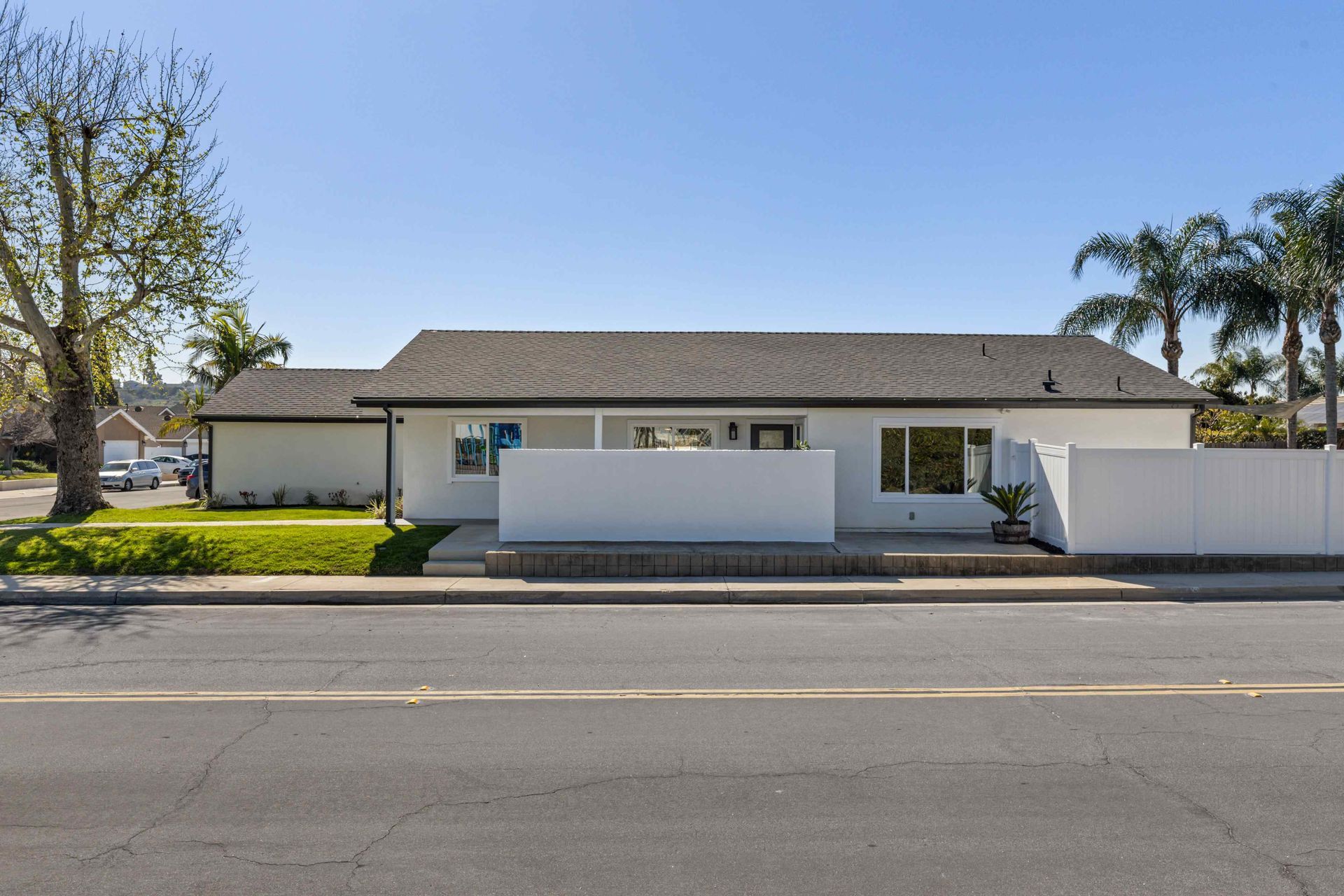 White house with grey roof, small front yard, palm trees, and blue sky.