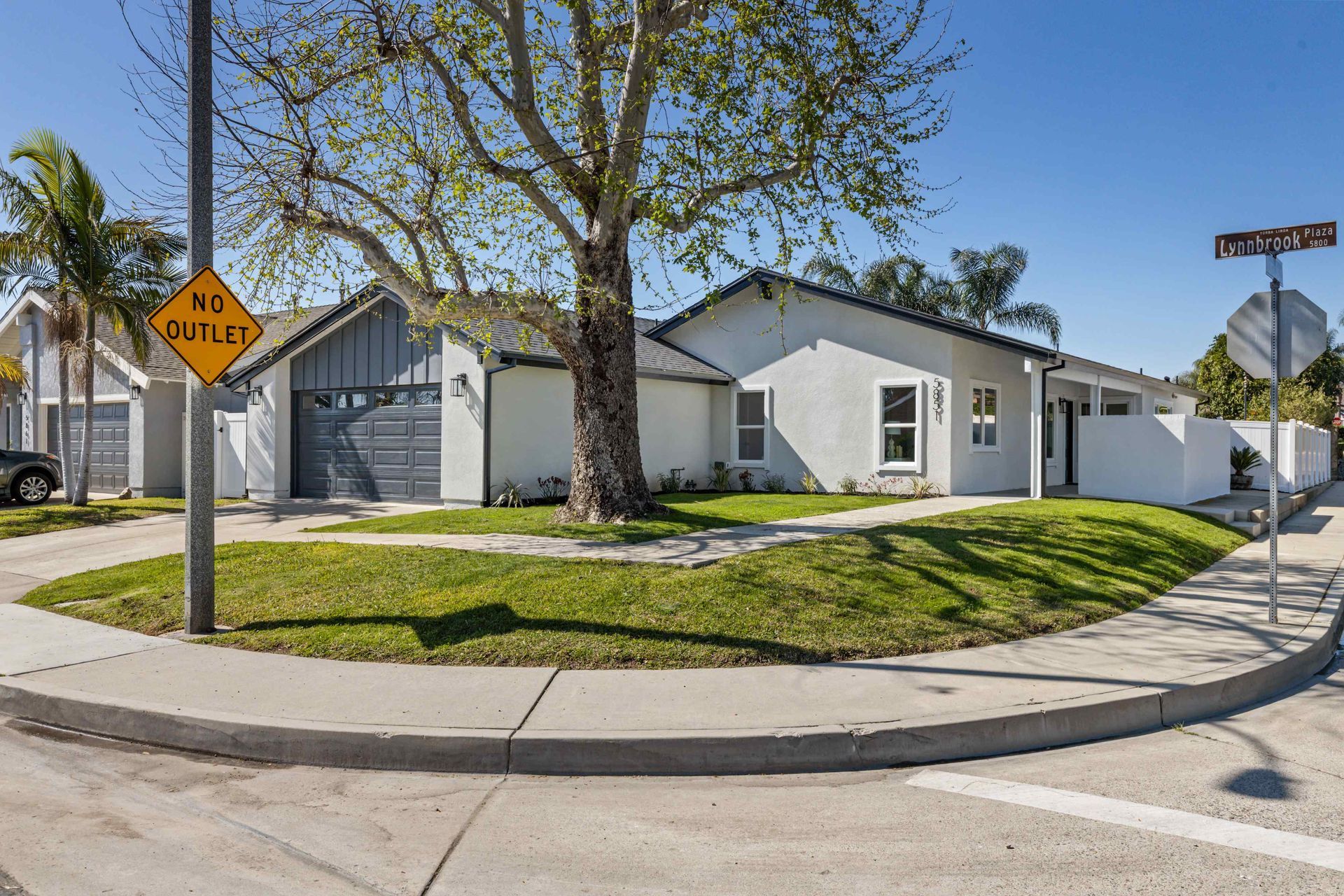 Modern white house on a corner lot with green lawn, street signs, and a gray garage door.