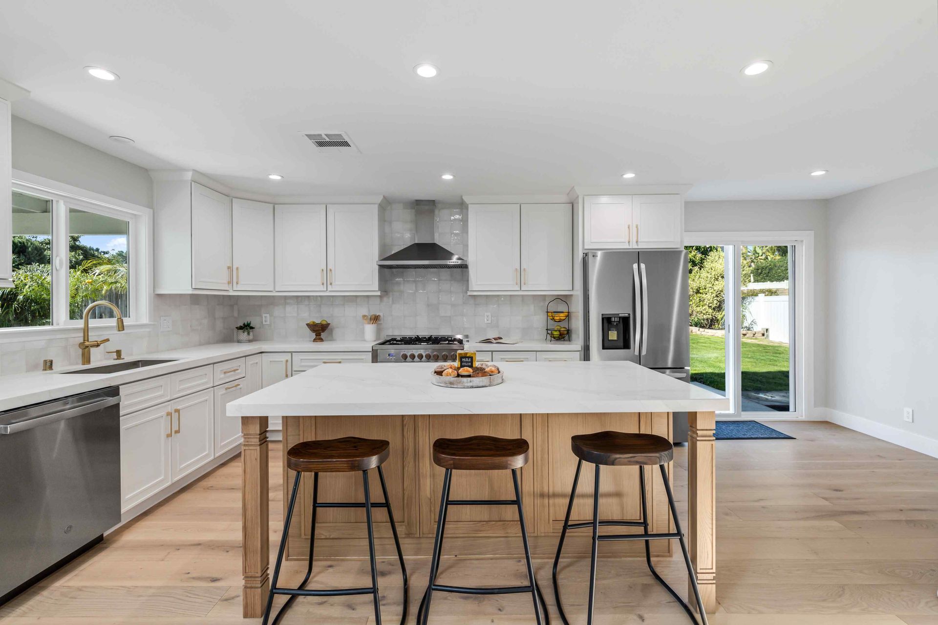Bright, modern kitchen with white cabinets, wood island, and stools; stainless steel appliances and outdoor view.