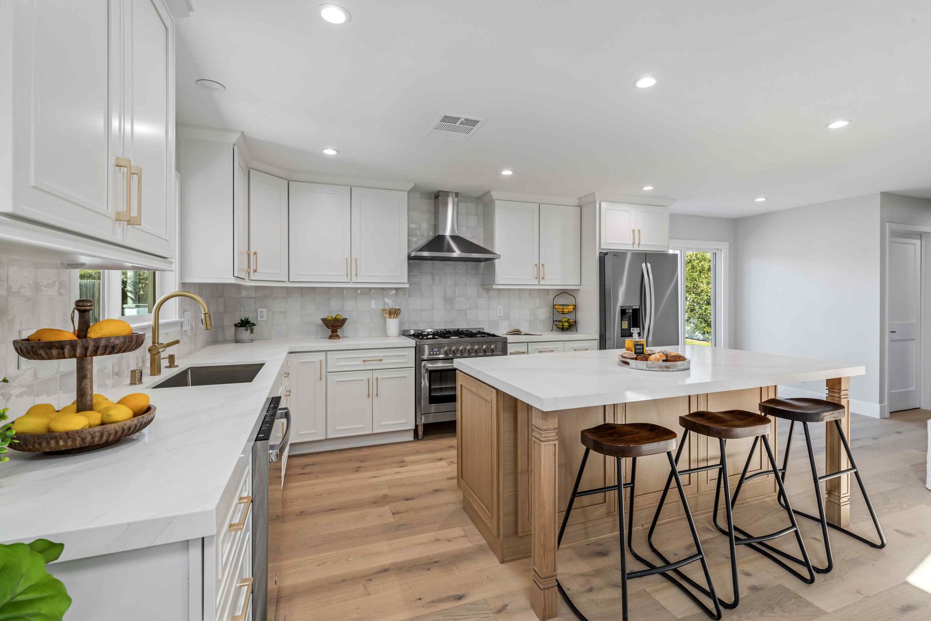 Modern white kitchen with island, wood floors, and stools.