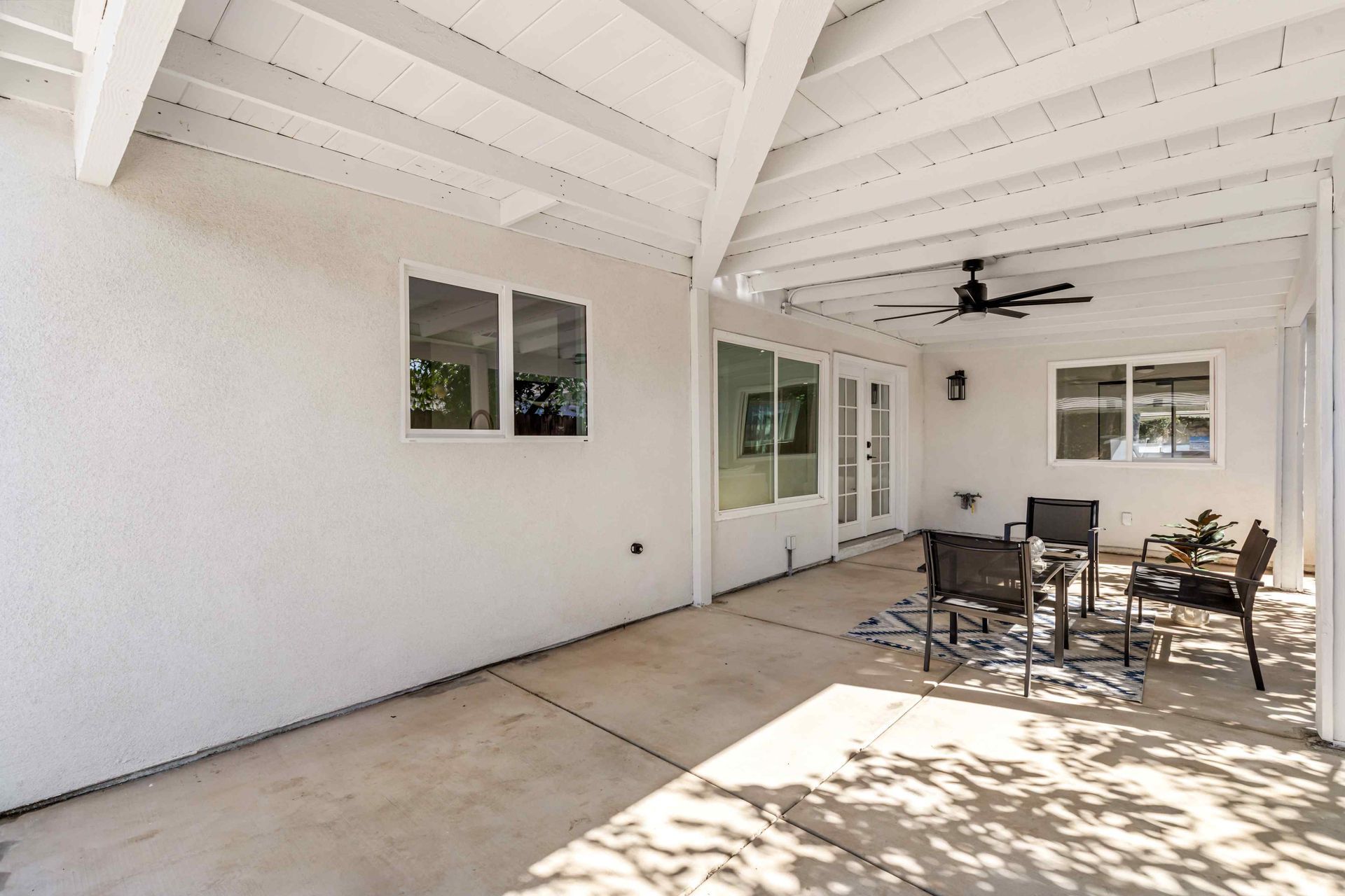 Covered patio with white walls, ceiling beams, and outdoor furniture.