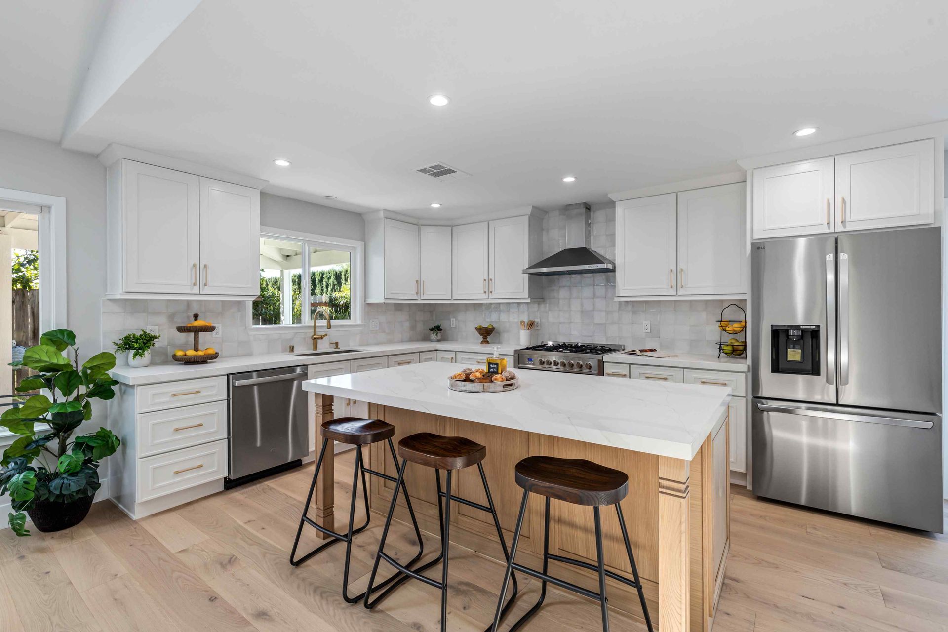 Modern white kitchen with island, stainless steel appliances, and wood floors.