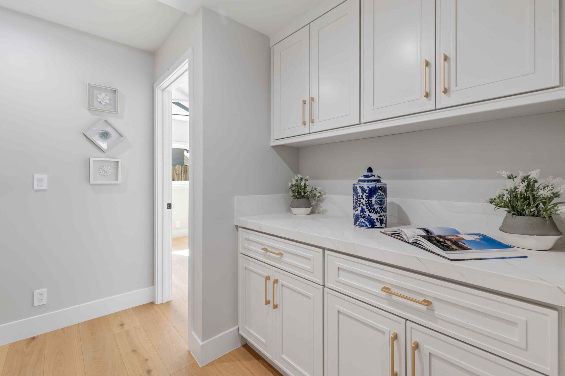 White cabinets with gold handles, light gray walls, wood floor, and doorway.