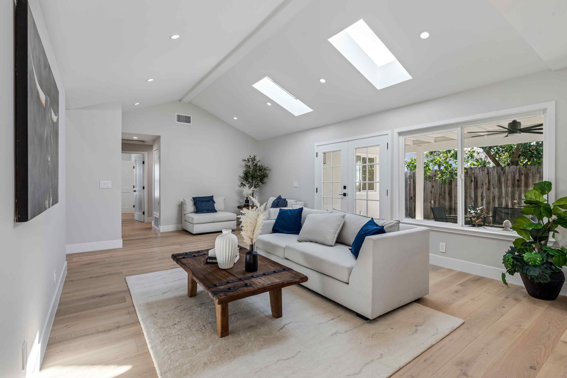 Bright living room with light wood floors, white sofa, skylights, and a view to the outdoors.