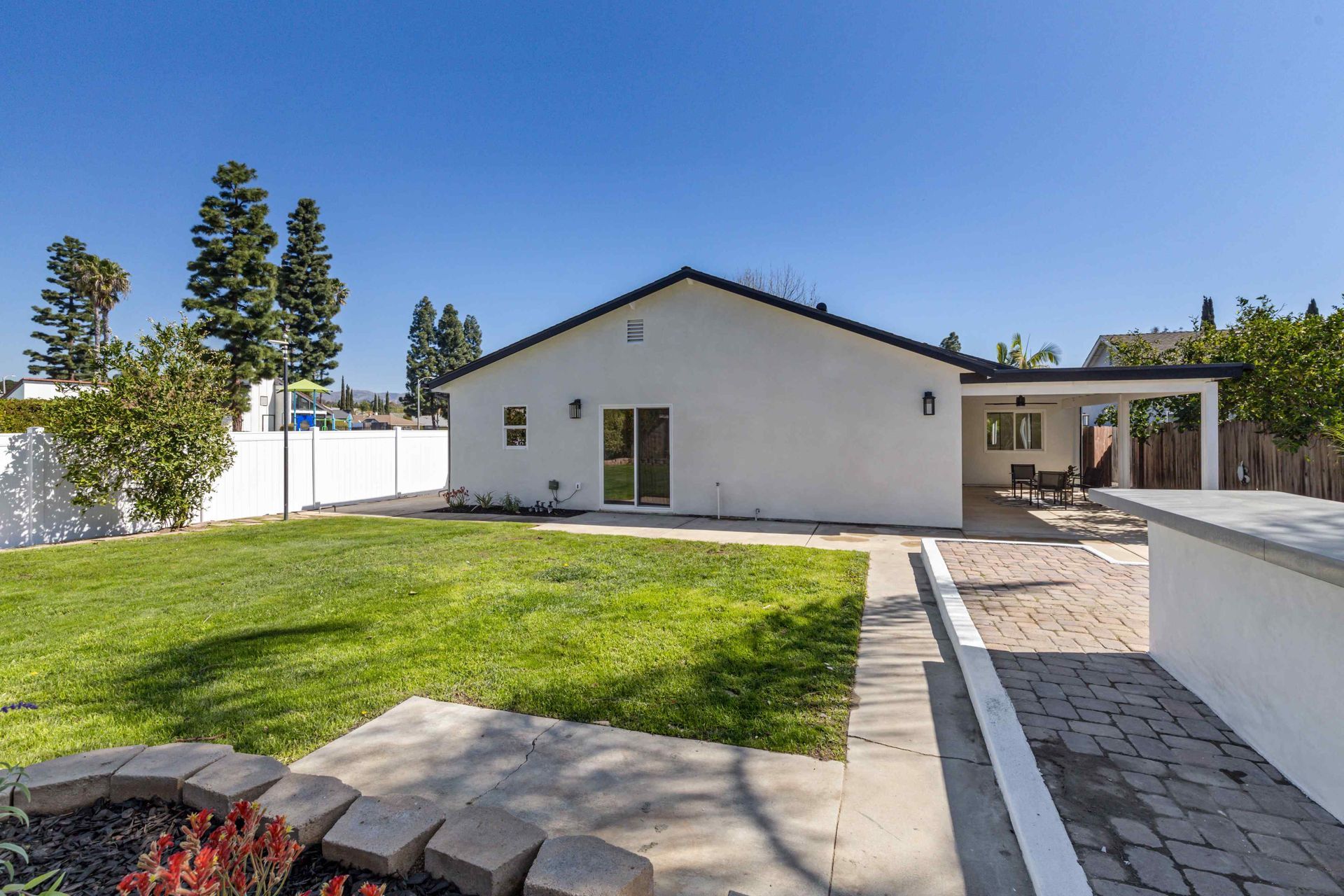 Backyard of a white house with green grass, patio, and blue sky.
